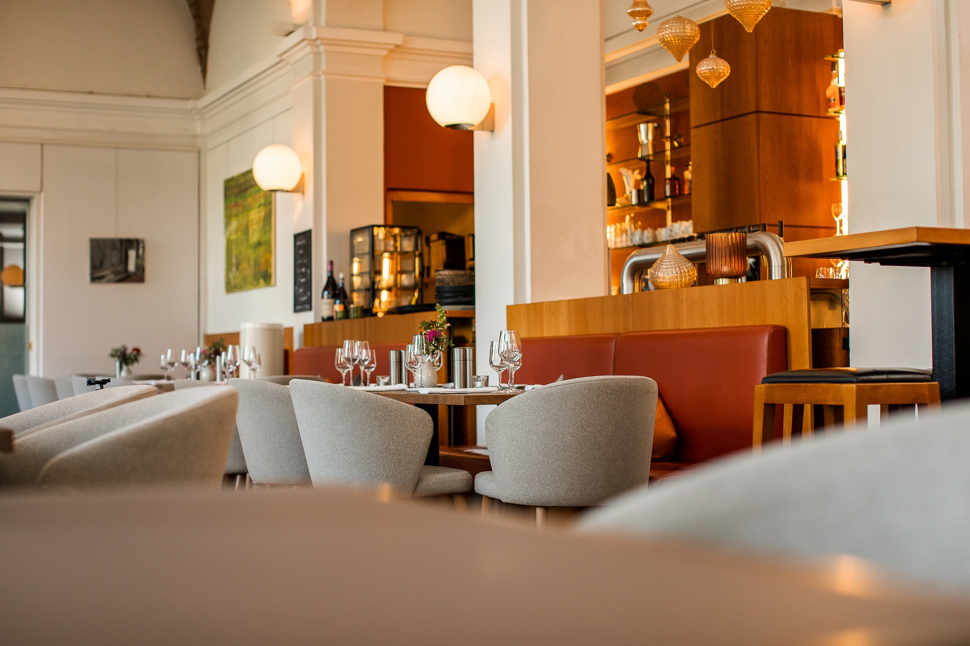Ein modernes Restaurantinterieur mit runden Tischen, gedeckt mit Glaswaren, umgeben von hellgrauen Stühlen, und einem Barbereich im Hintergrund.